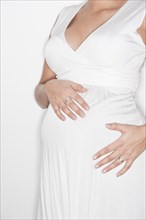 Pregnant woman in a white dress holding her hands on her belly