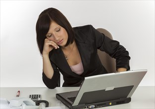 Young woman with a laptop sitting at a desk and sleeping