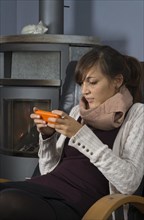 A young woman of Indonesian origin is sitting in front of a wood burner working on a smartphone