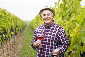 Winemaker or vintner standing with a glass of red wine in his vineyard