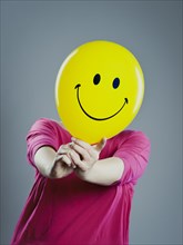 Woman with a smiley face balloon in front of her face