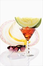Melon slice on cocktail glass in front of sun hat with sunglasses