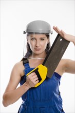 Woman wearing blue overalls and a protective helmet holding a saw
