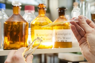 A laboratory worker using a pipette to fill a chemical liquid in a glass container
