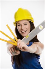 Woman wearing blue overalls and a hardhat holding a folding carpenter's ruler and a spirit level