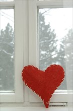 Red fabric heart leaning on an old window with a white frame