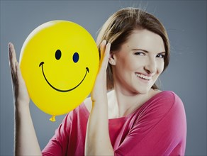 Smiling young woman holding a smiley face balloon