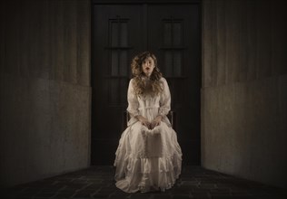 Young girl wearing a white dress sitting in front of a dark door