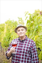 Winemaker or vintner standing with a glass of red wine in his vineyard