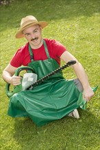 Gardener holding a hedge trimmer while sitting on the lawn