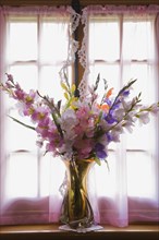 Glass vase with silk flowers on the window sill of an old reconstructed 1983 Canadiana cottage style residential log home