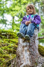 Little girl sitting on a tree stump in the forest