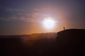 Man standing on the edge of a cliff at sunset