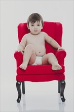 Young boy wearing a diaper sitting on a red chair