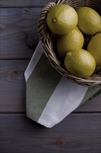 Lemons in a basket on a kitchen towel on a wooden background