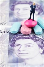 Miniature figurine of businessman standing on medical pills on pound banknote