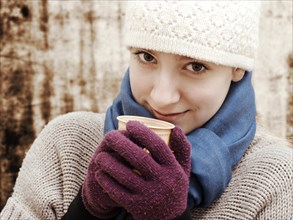 Girl wearing a hat and a scarf holding a cup