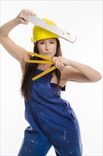 Woman wearing blue overalls and a hardhat holding a folding carpenter's ruler and a spirit level