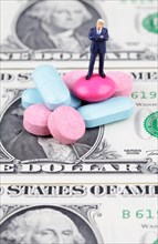 Miniature figurine of businessman standing on medical pills on US dollar bill