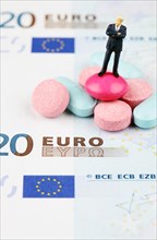 Miniature figurine of businessman standing on medical pills on euro banknote