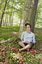 Young man sitting in front of a tree in the woods