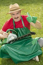Gardener holding a hedge trimmer while sitting on the lawn