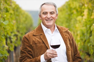Winemaker or vintner standing with a glass of red wine in his vineyard