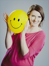 Smiling young woman holding a smiley face balloon