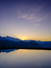 Mountain silhouettes are reflected in an artificial mountain lake at sunset