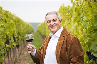 Winemaker or vintner standing with a glass of red wine in his vineyard
