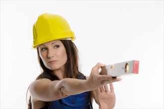 Woman wearing blue overalls and a hardhat holding a spirit level