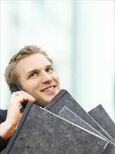 Businessman carrying ring binders while using a mobile phone