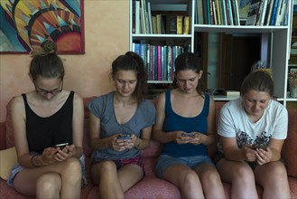 Four young woman sitting on a sofa chatting with their smartphones