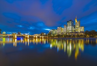 Skyline of Frankfurt with illuminated skyscrapers and Untermainbrucke bridge with water reflections in Main