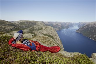 Young woman in a red sleeping bag with view over the fjord