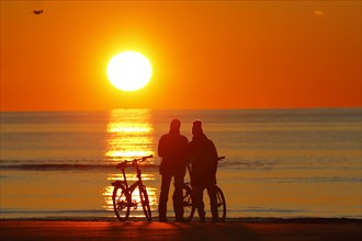 Couples with bikes on the beach watching the sunset