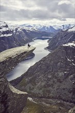 Woman sits on a rock platform on the Trolltunga and looks over fjord landscape