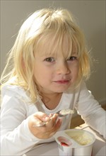 Little blond girl eating yoghurt