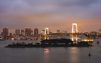 View of skyline with skyscrapers and illuminated Rainbow Bridge in the evening