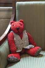 Knitted red teddy bear with vest on striped armchair