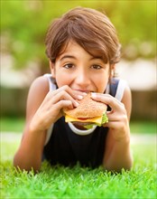 Teen boy eating burger outdoors