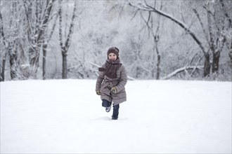 Girl in winter clothes runs across snowy meadow in winter