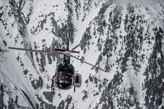 Helicopter in front of snow-covered rock face