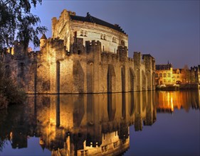 Illuminated castle Gravensteen at dusk with water reflection