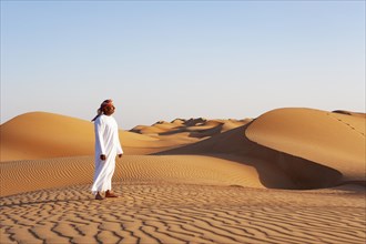 Bedouin in traditional clothing stands in the sand desert