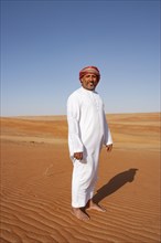 Bedouin in traditional dress stands in the sandy desert