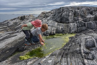 Boy and girl playing between rocks with algae