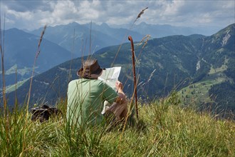 Hiker resting on alpine meadow with a view of the Lesach Valley and the Carnic Alps