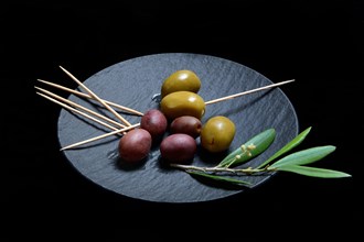 Black and green olives with toothpick on black plate