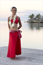 Native young woman with flower decoration stands on jetty by the water